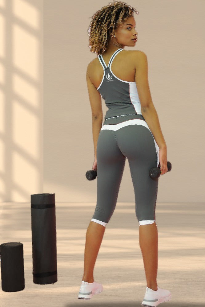 Legging capri gris à bords blancs aux genoux, porté avec un débardeur gris. Le modèle tient deux haltères.