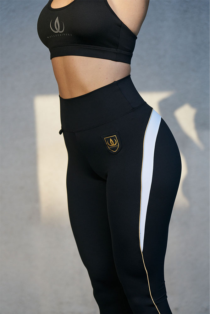 Le legging noir présente un écusson doré à la hanche et une rayure blanche bordée d'or sur le côté.