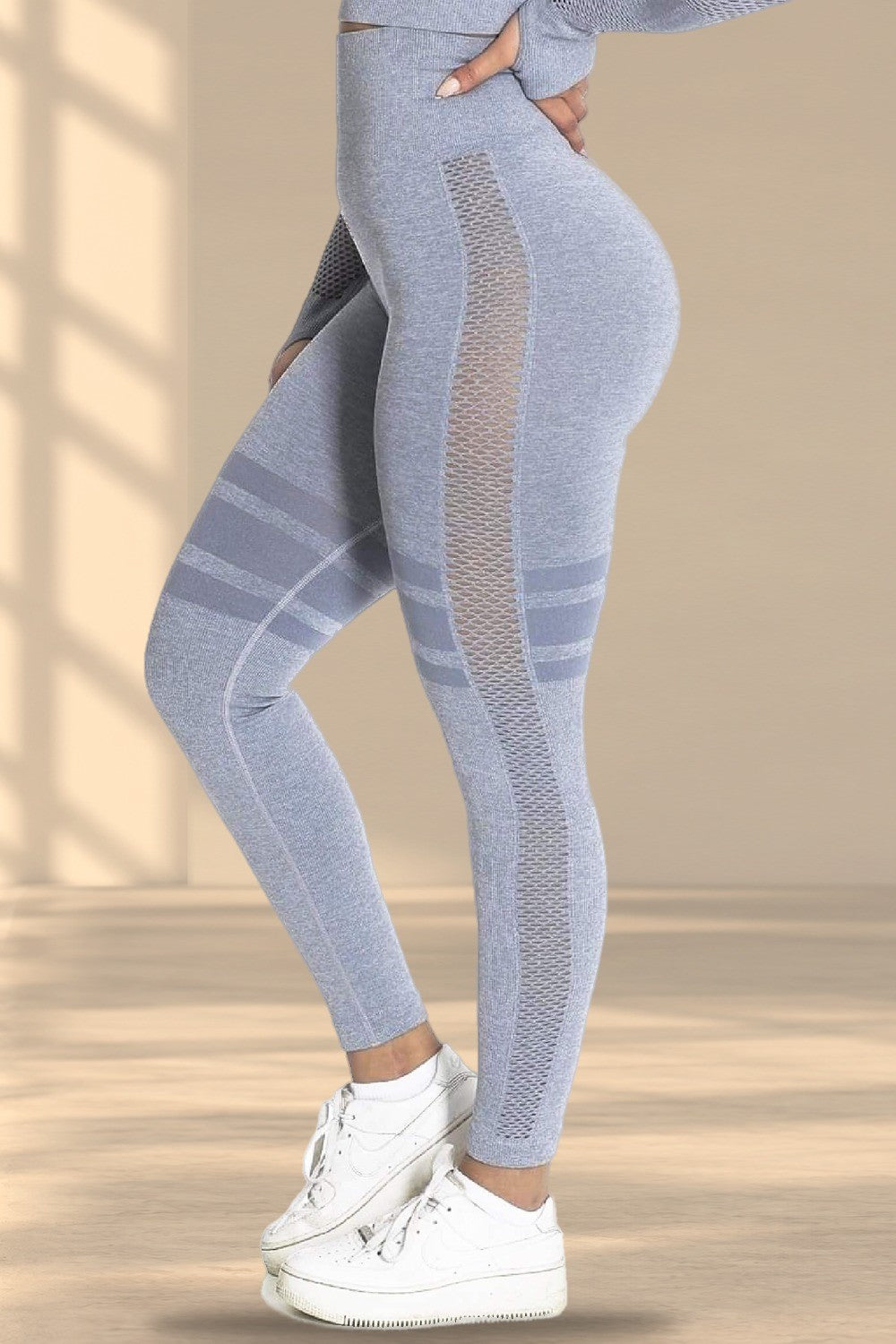 Le côté du legging gris avec empiècement en mesh et bandes rayées, au-dessus de baskets blanches.