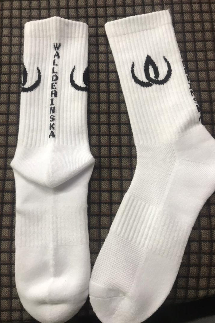 Ein Paar weiße Socken mit schwarzem Logo und Emblem entlang des Schafts, vor dunklem Untergrund.