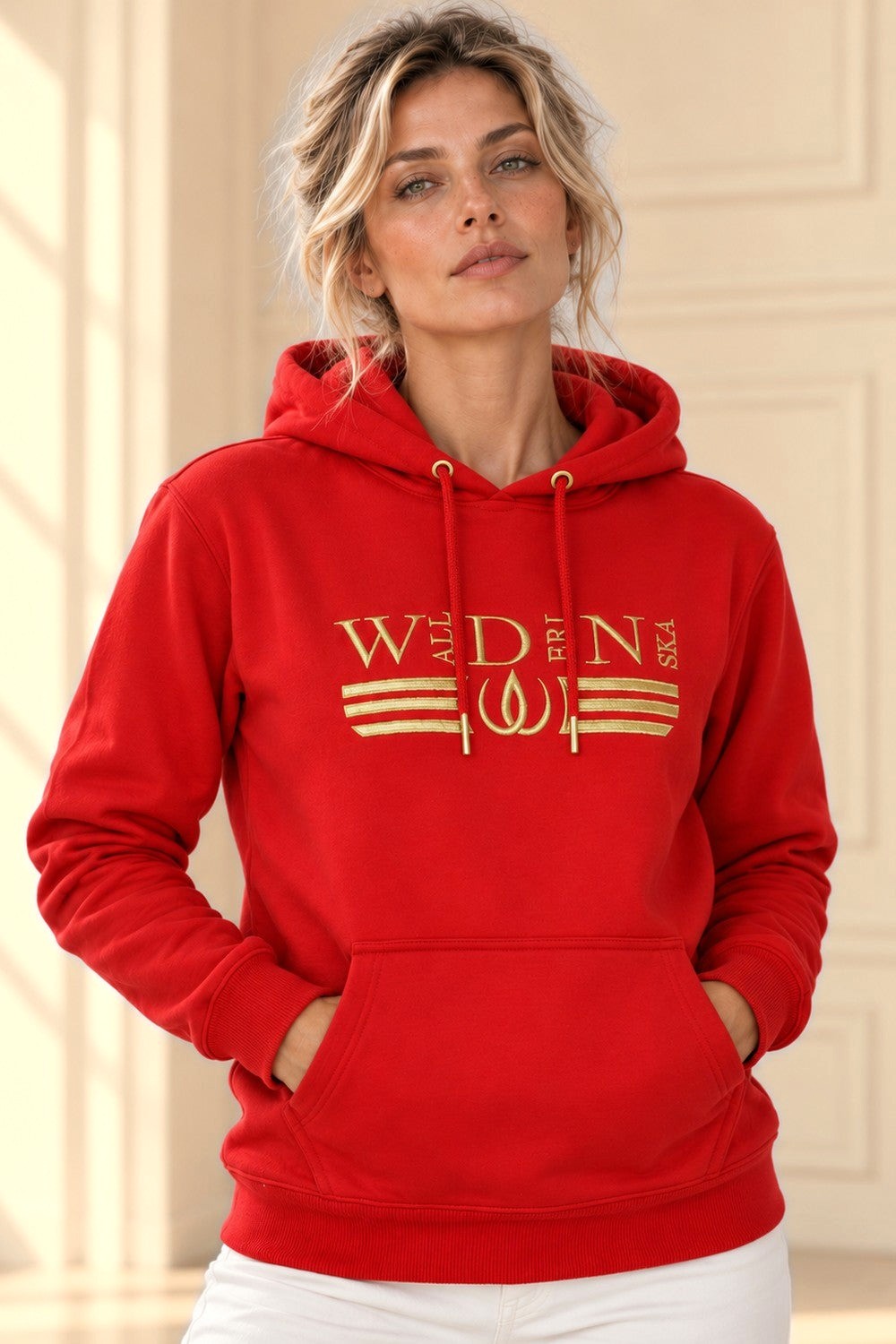 Röd Deluxe Hoodie med guldbroderad logga och guldränder över bröstet, buren till vita byxor.