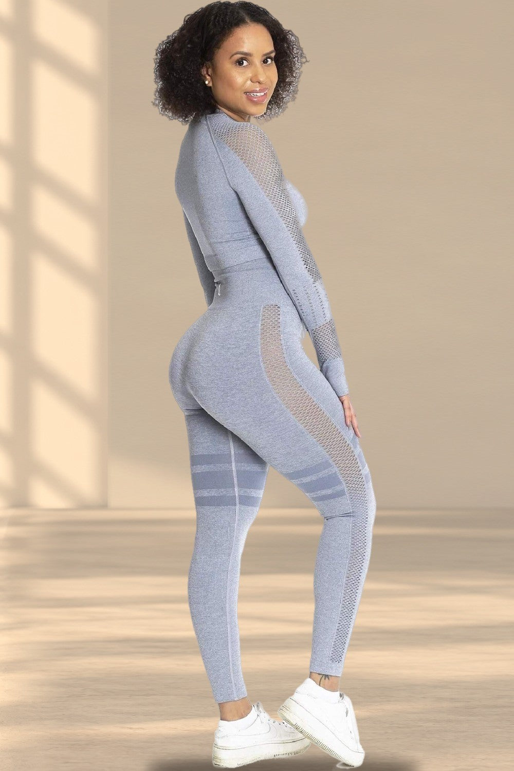 Le haut se porte avec un legging gris assorti et des baskets blanches. Le modèle regarde par-dessus son épaule.