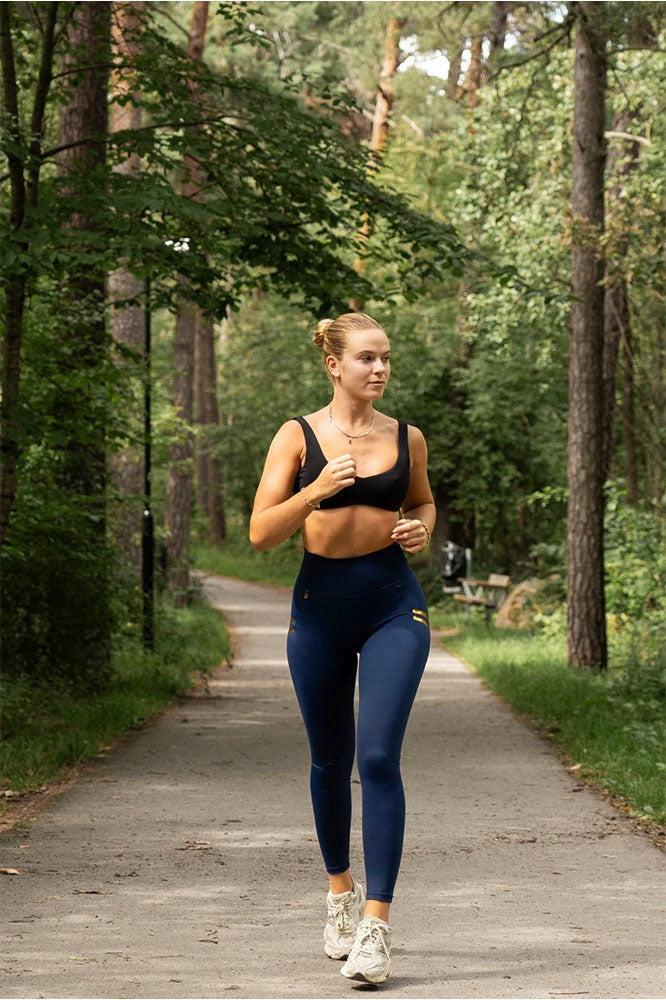 Corsa su un sentiero nel bosco con leggings navy a righe oro e reggiseno sportivo nero.