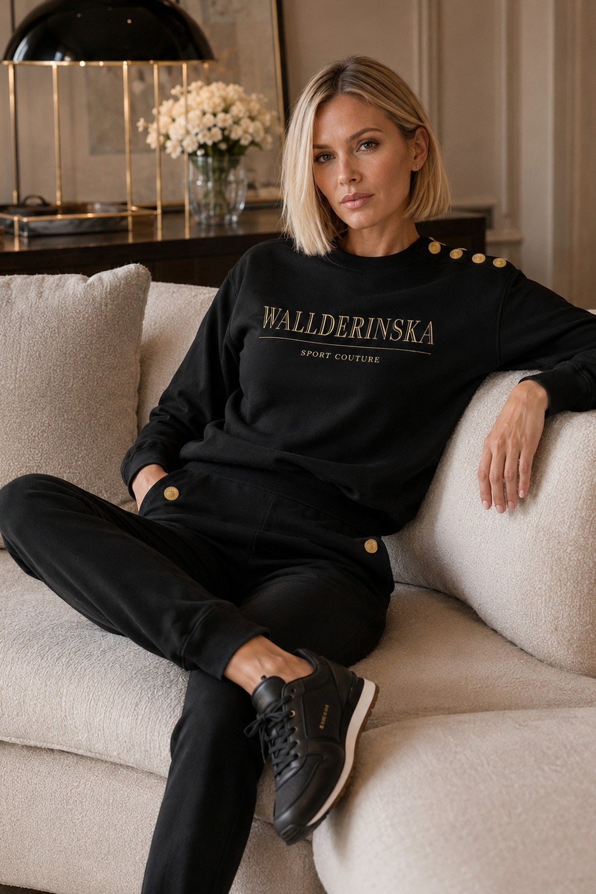 Das Edge Gold Button Set in Schwarz, mit vier Goldknöpfen an der Schulter, auf einem hellen Sofa.