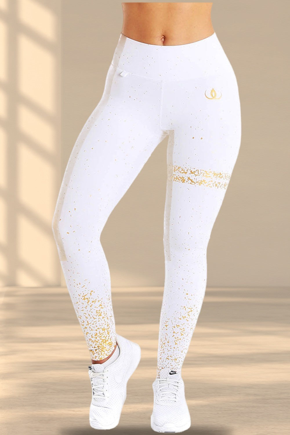 Legging blanc avec des éclaboussures dorées sur le tissu, une bande dorée sur la cuisse et un logo doré à la hanche.