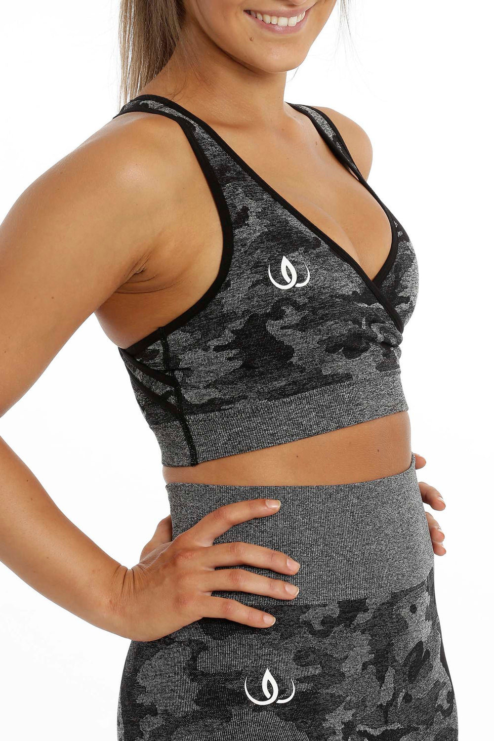 Das Top schräg von der Seite gesehen, mit weißem Logo auf der Brust, über der Leggings im gleichen Camouflage.