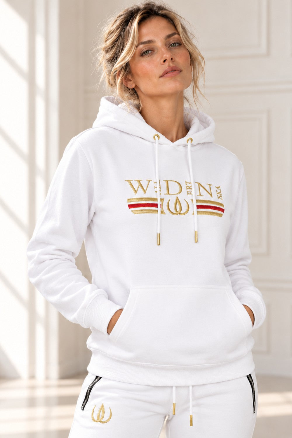 Vit Deluxe Hoodie med guldbroderad logga, rött och guldfärgat streck över bröstet och snören med guldspetsar.