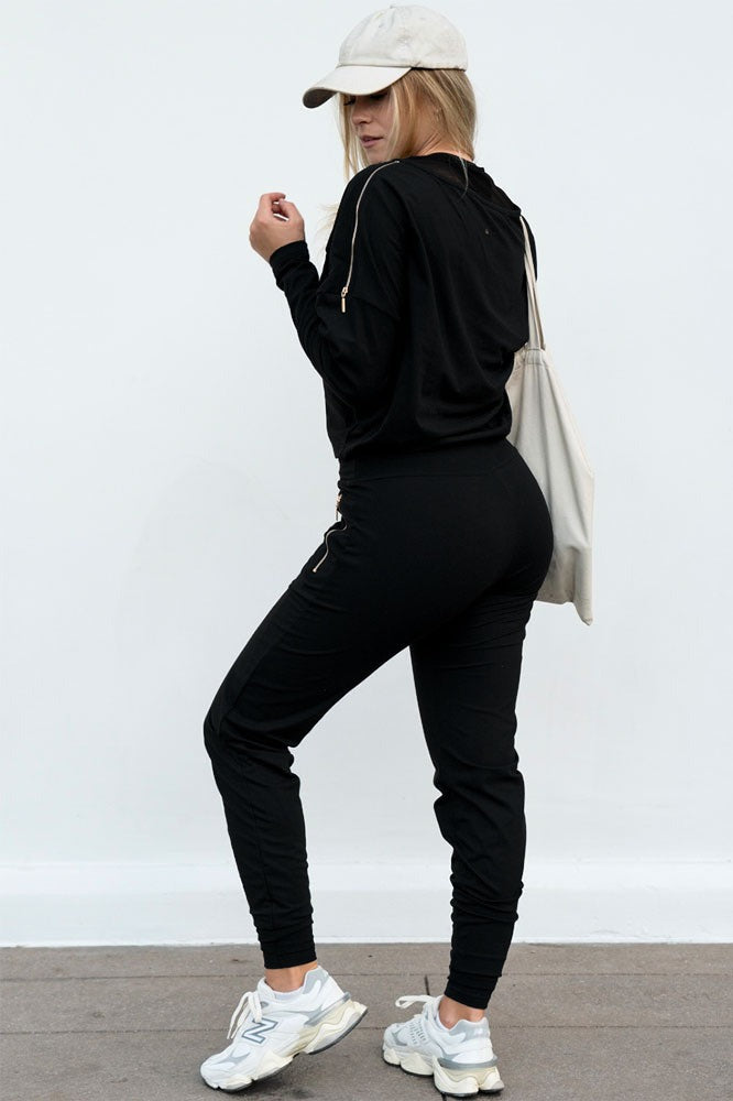 Le pantalon avec un pull noir, une casquette et un tote bag. Une fermeture éclair dorée apparaît à l'épaule.