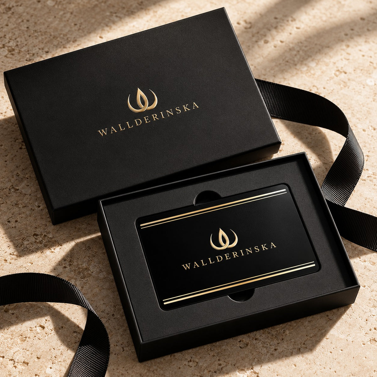 Carte cadeau Wallderinska en noir avec logo doré, dans une boîte noire avec un ruban de soie noir.